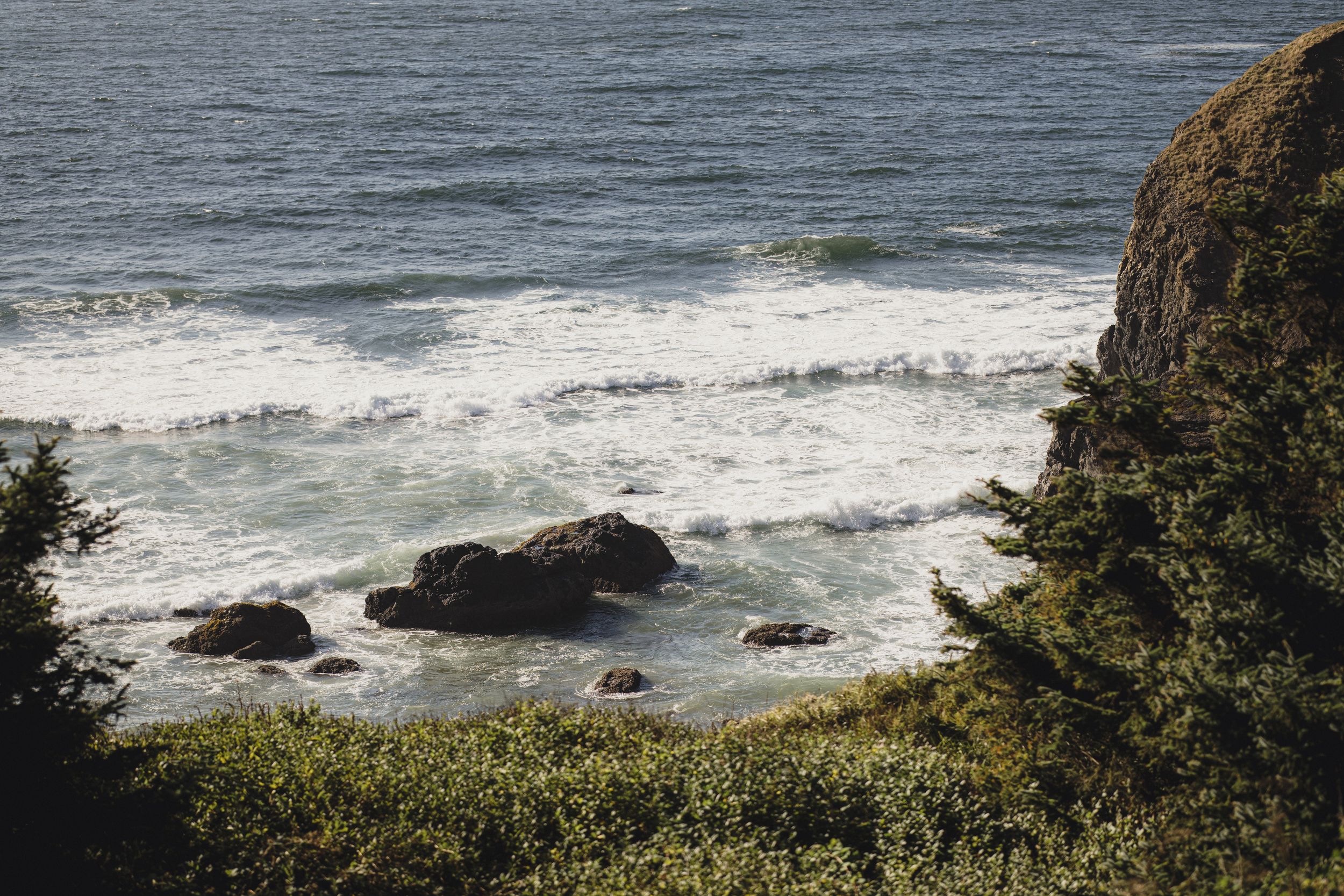 Scenic coastal view with waves crashing over rocks along a rugged shoreline with lush green cliffs.
