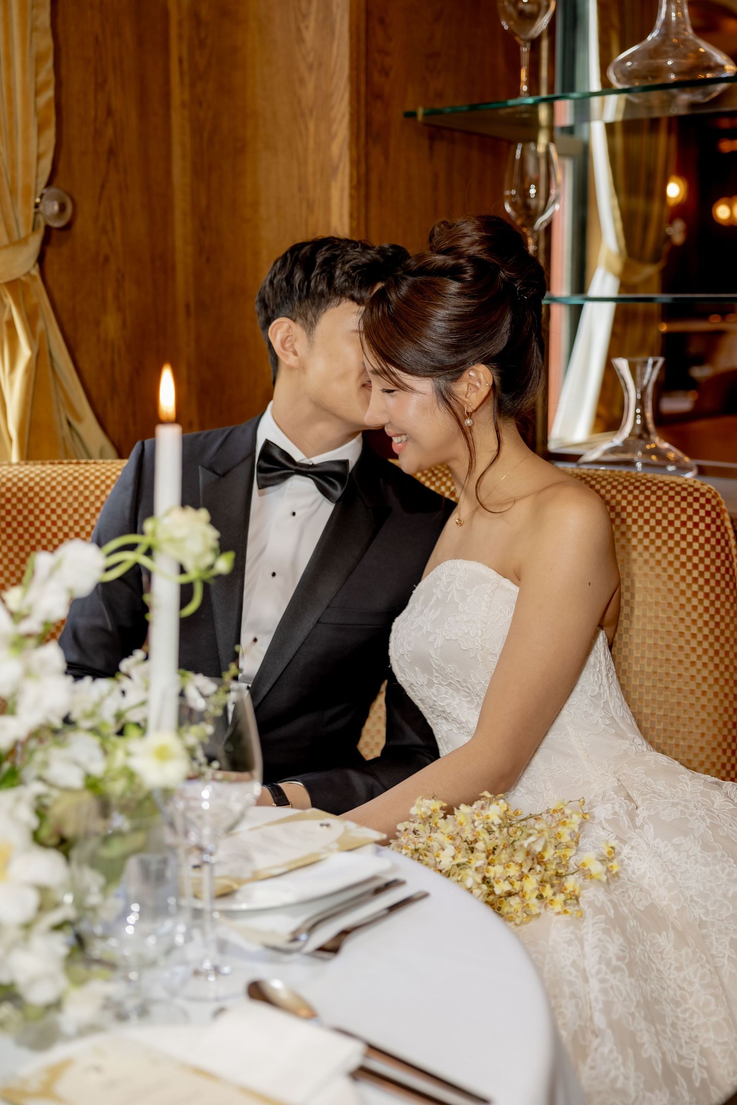 An elegant newlywed couple in wedding attire share an intimate moment at a candlelit table at The Golden Swan Restaurant in New York City.