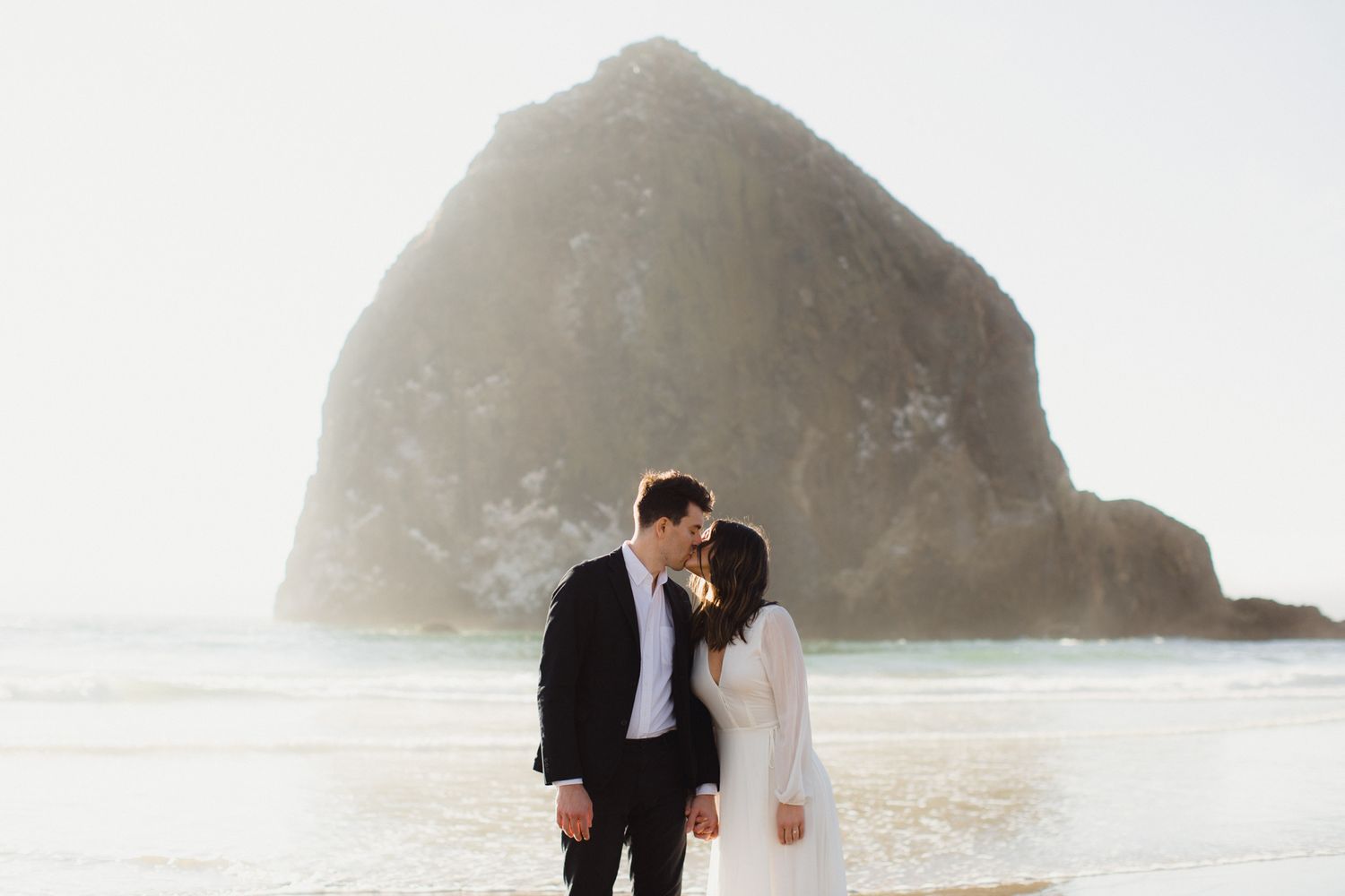 Couple sharing a romantic kiss on the beach with iconic Haystack Rock in the background at Cannon Beach, Oregon.