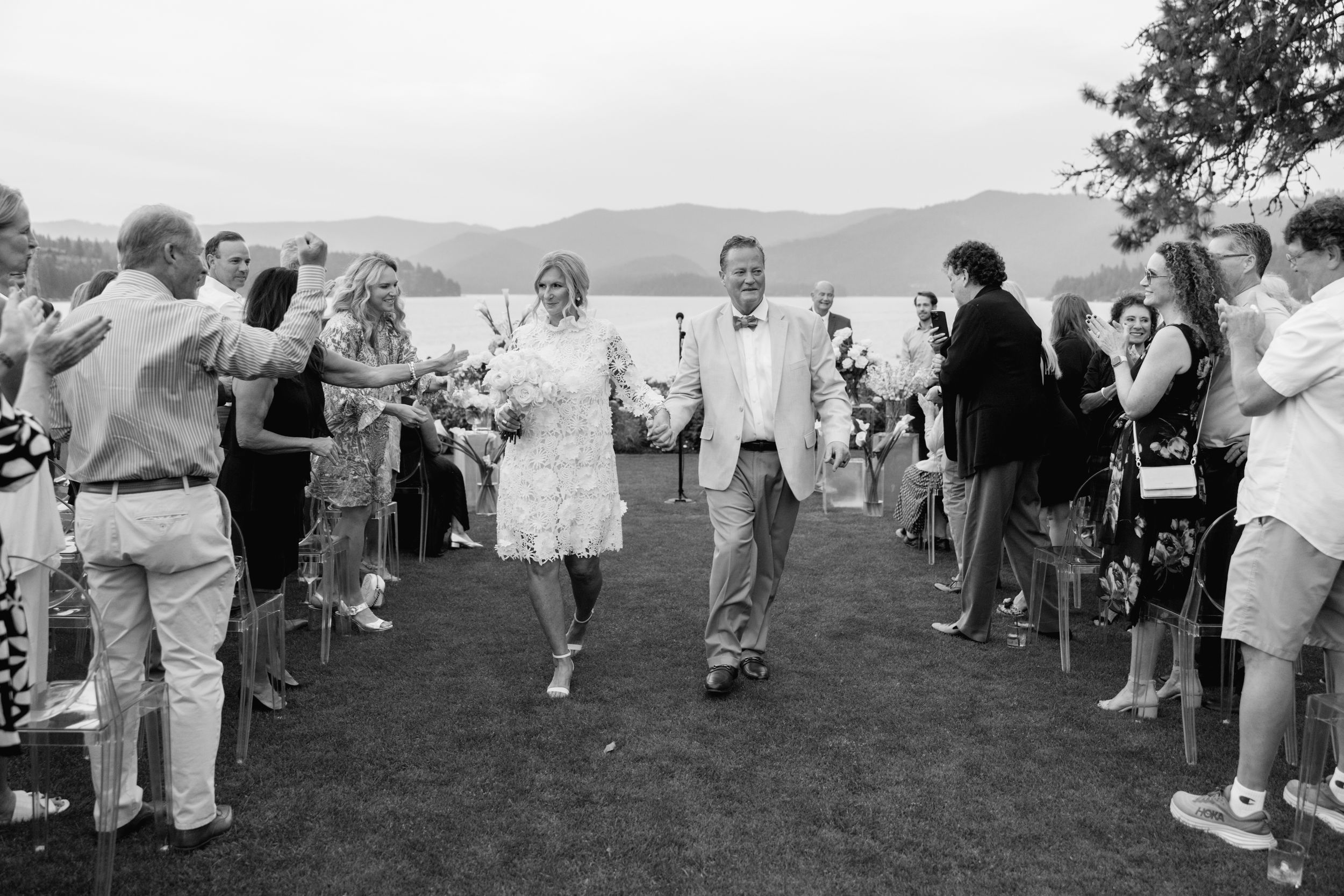 Newlywed couple walks down the aisle as guests celebrate at an outdoor lakeside wedding ceremony.