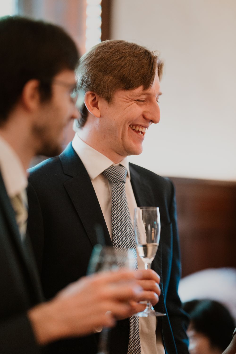 A smiling man in a dark suit and striped tie holds a champagne glass at a formal event.