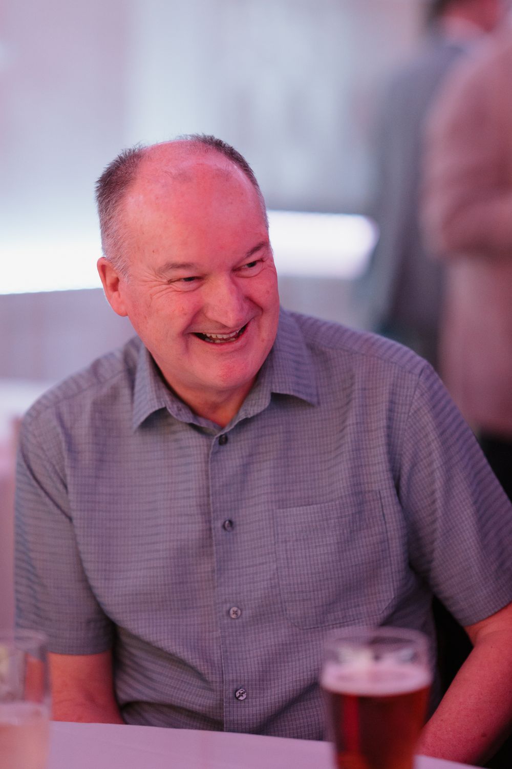 Smiling middle-aged man in a gray shirt enjoying a drink at a social gathering.