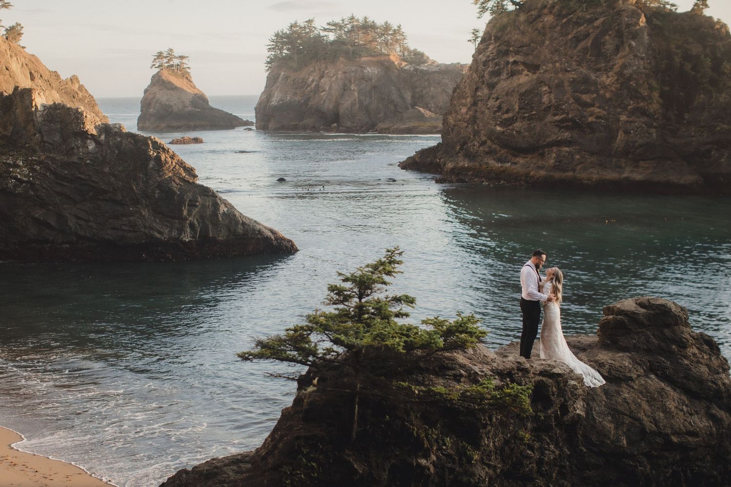 Couple in wedding attire embracing on a misty Oregon coast beach with dramatic sea stacks in the background.