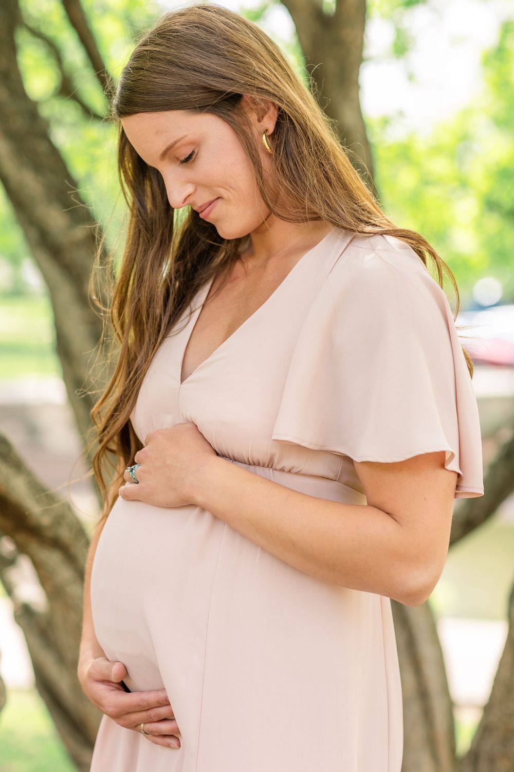 Candid moment of a mama smiling gently while holding her baby bump outdoors