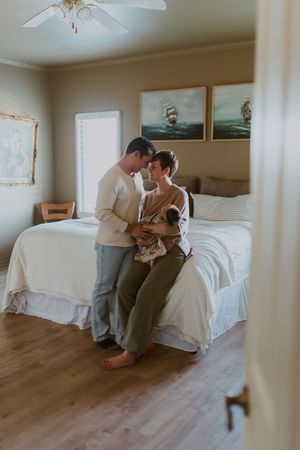 Couple sharing tender moment with newborn baby in a cozy bedroom with nautical artwork.