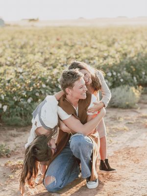Mother in vest and jeans embracing two children in a blooming cotton field at sunset.