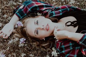 Young woman with long hair lying in a field of wildflowers wearing a plaid flannel shirt outdoors.