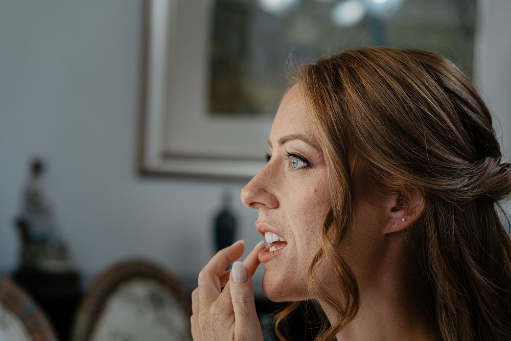 Close-up of bride touching her lips during wedding morning makeup preparation indoors.