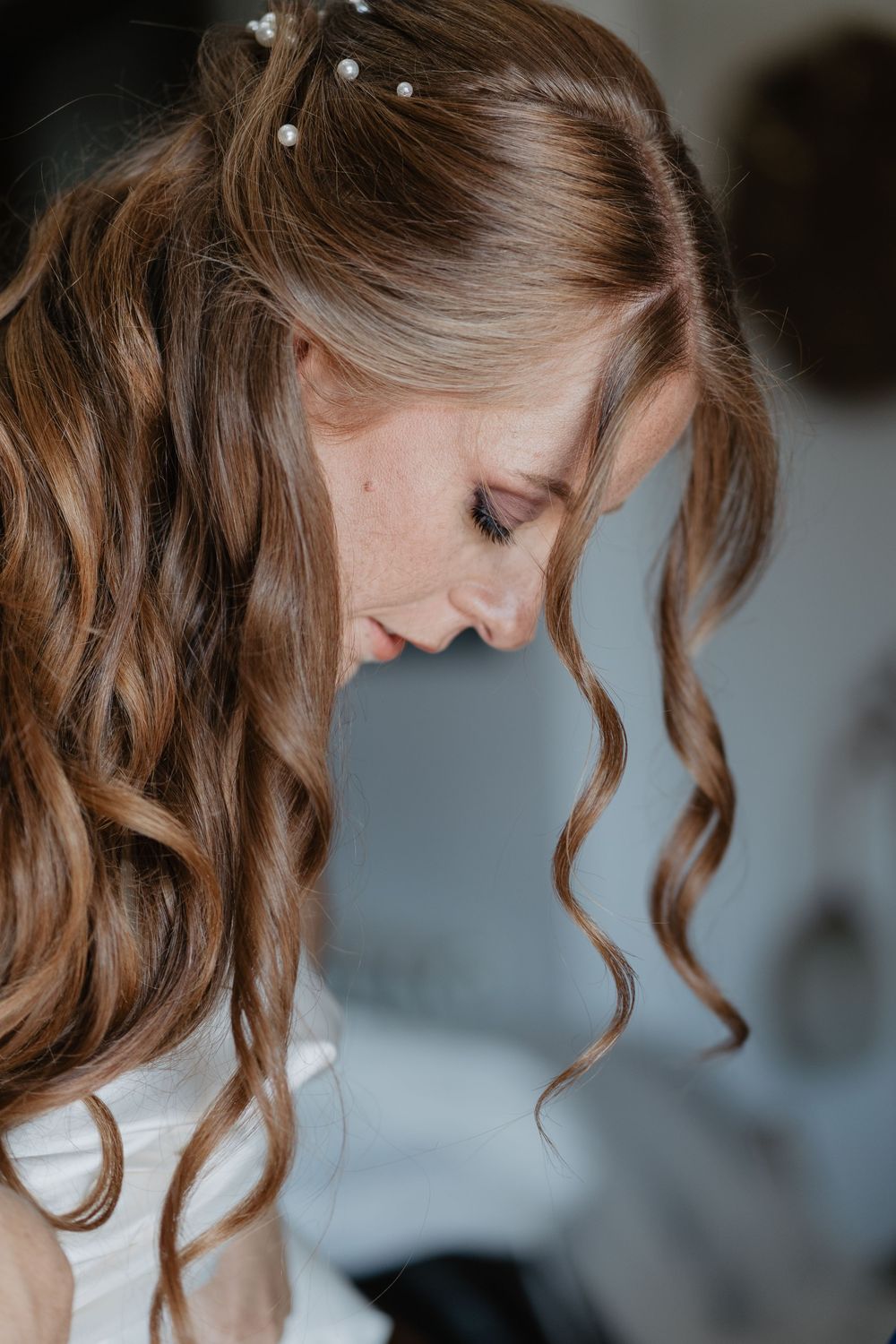 Close-up portrait of bride with elegant half-up curly hairstyle adorned with pearl hair pins.