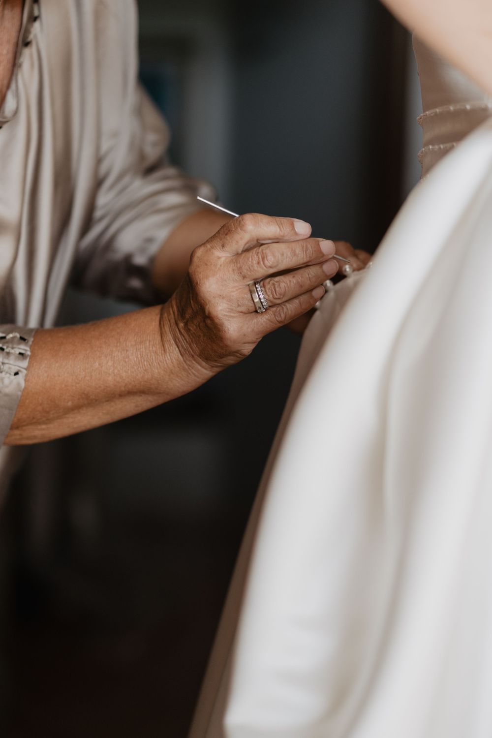 Close-up of older woman's hands fastening buttons on bride's white wedding dress.
