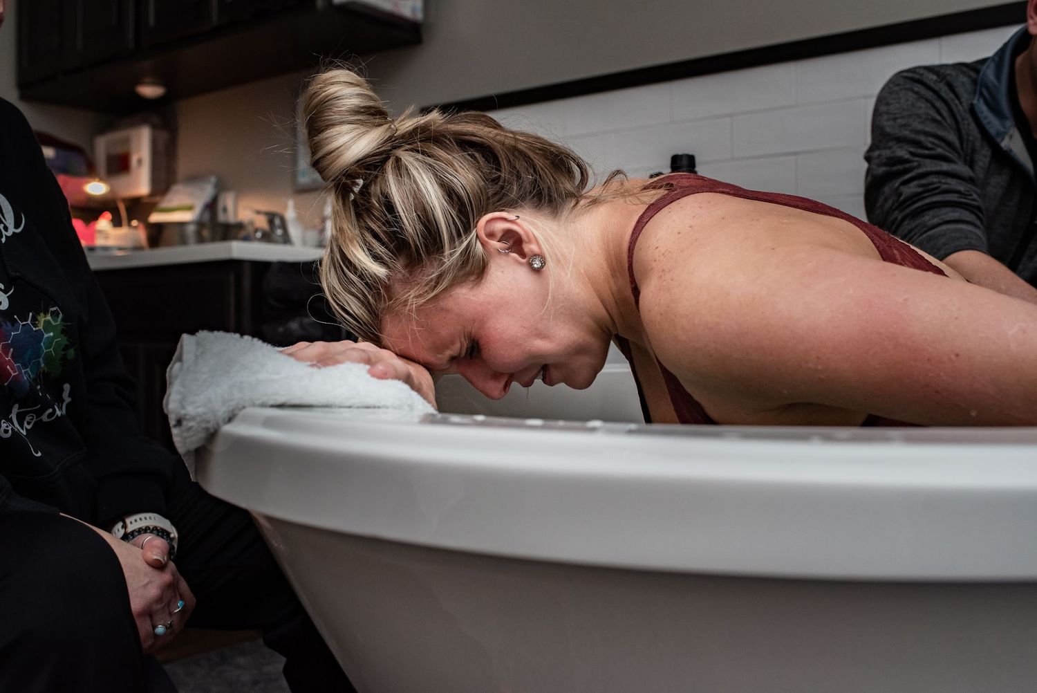 A laboring person leans over the edge of a white birthing tub during active labor.