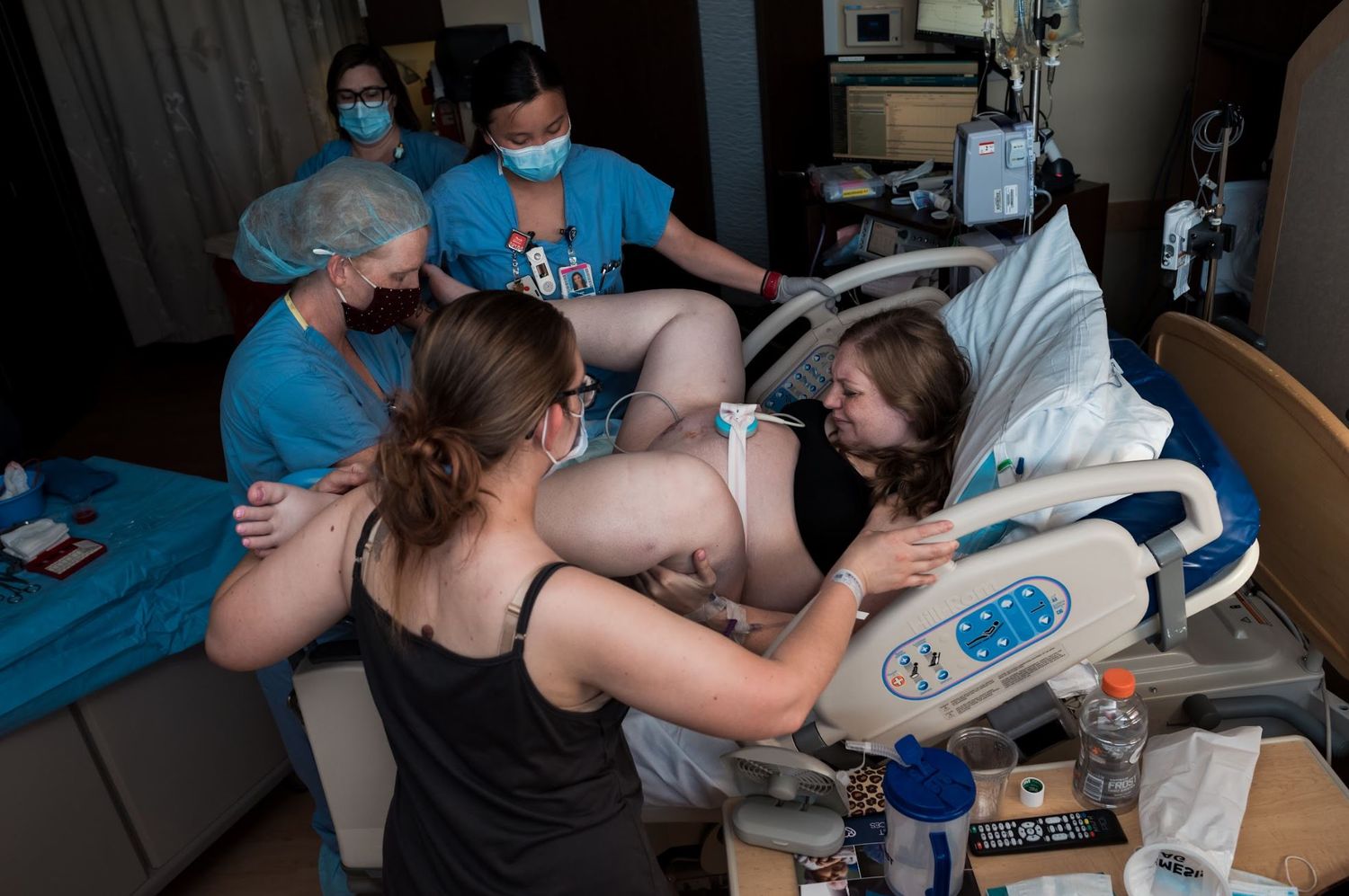Medical team assists during childbirth with monitoring equipment visible in hospital room.