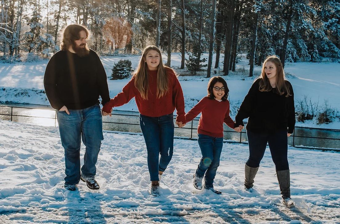 A group walks together and holds hands while enjoying a snowy winter landscape with trees in the background.
