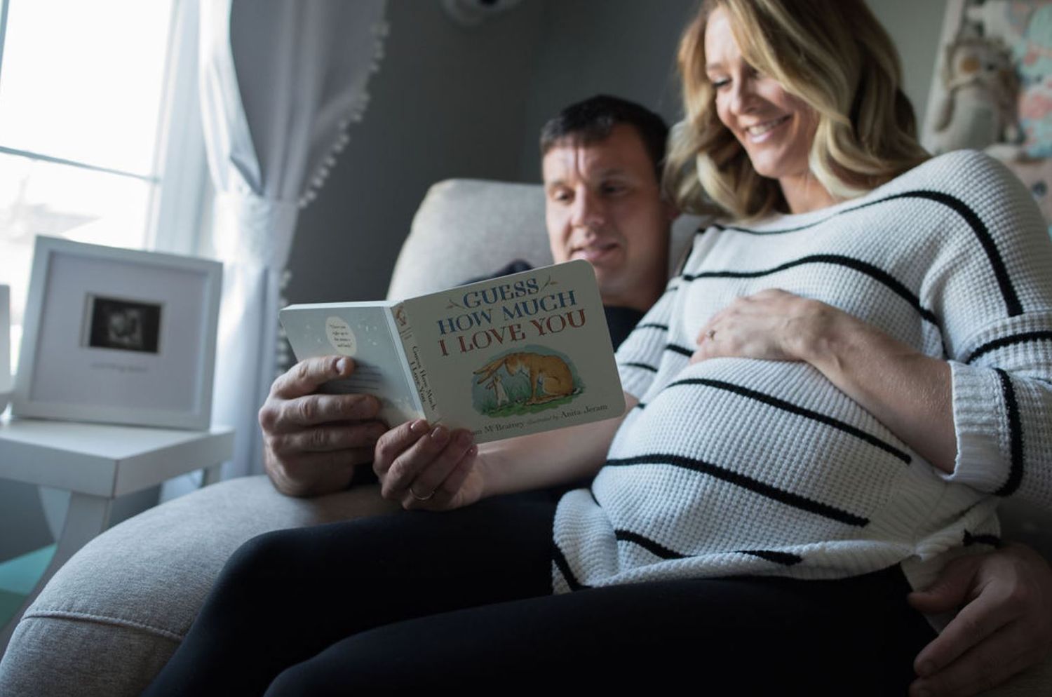 An expectant couple reads a pregnancy book together while relaxing on a couch.