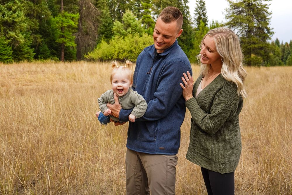 Happy family with father holding laughing baby and blonde mother in sunlit autumn field outdoors.