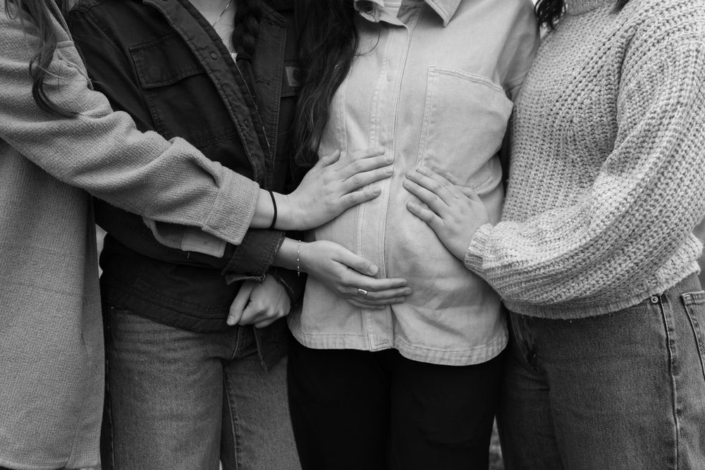 Black and white photo of three people placing hands on a pregnant woman's baby bump.