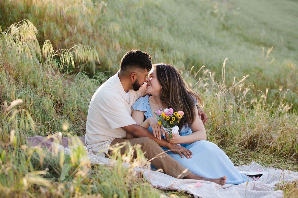 Couple sharing a romantic moment on a picnic blanket in a green meadow with wildflowers.