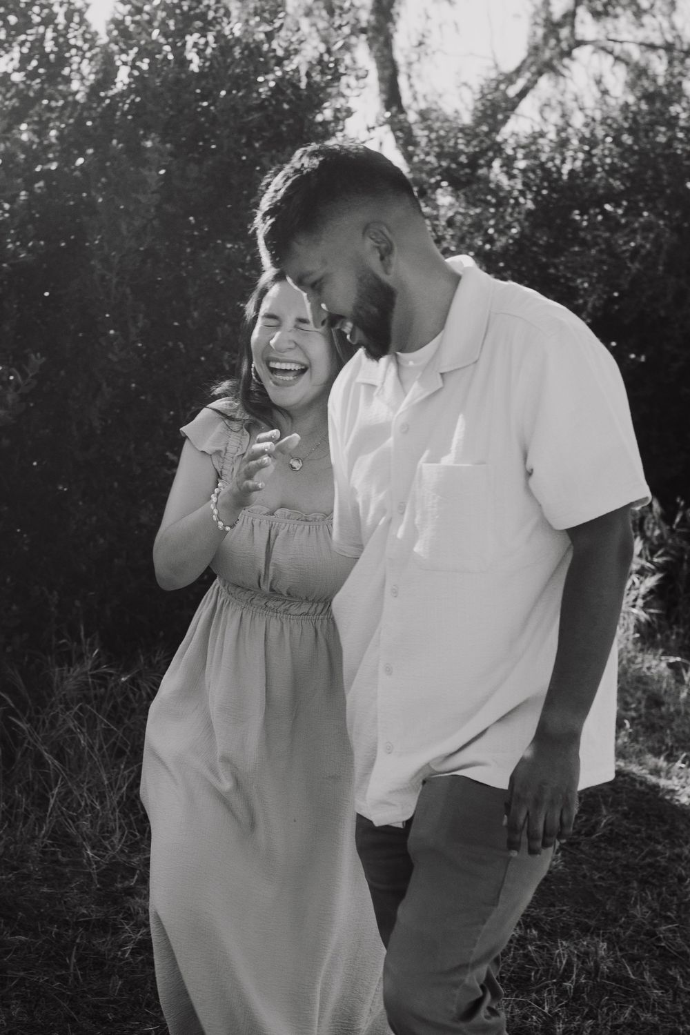 Happy couple laughing together outdoors in black and white engagement photo.