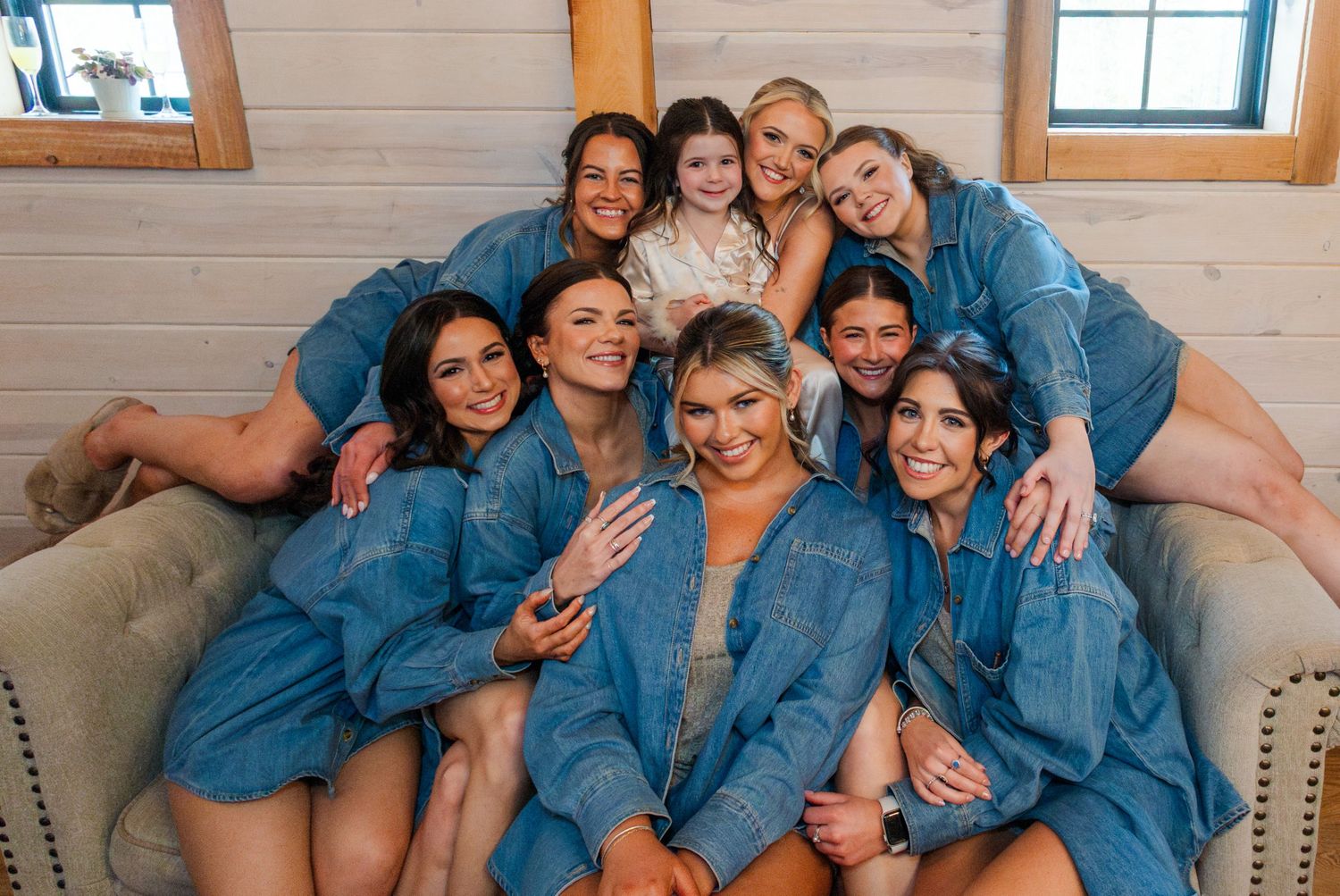 Group of bridesmaids in matching denim robes posing together on a couch with the bride before a wedding.