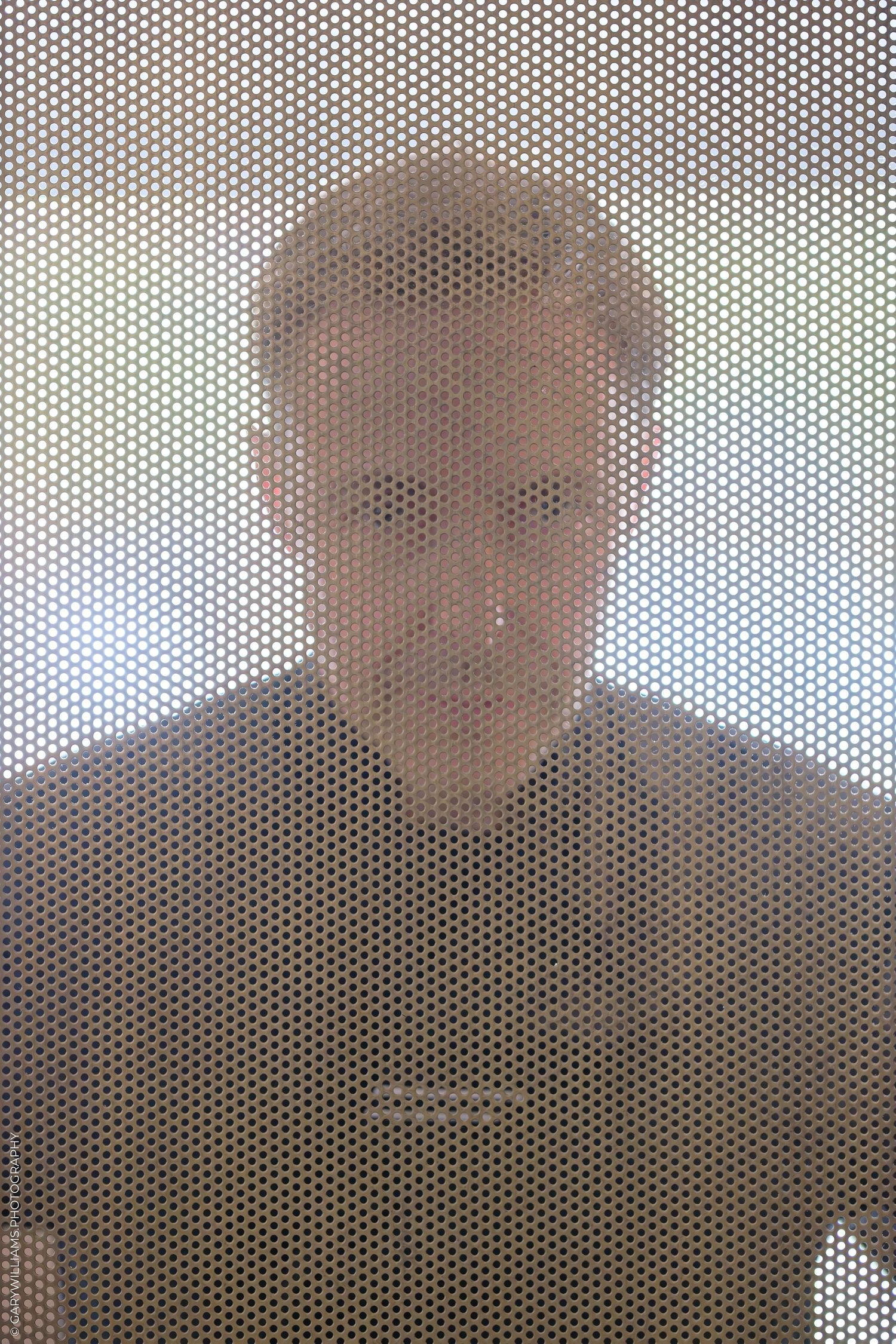 Man seen through perforated metal mesh screen creating abstract geometric pattern effect.