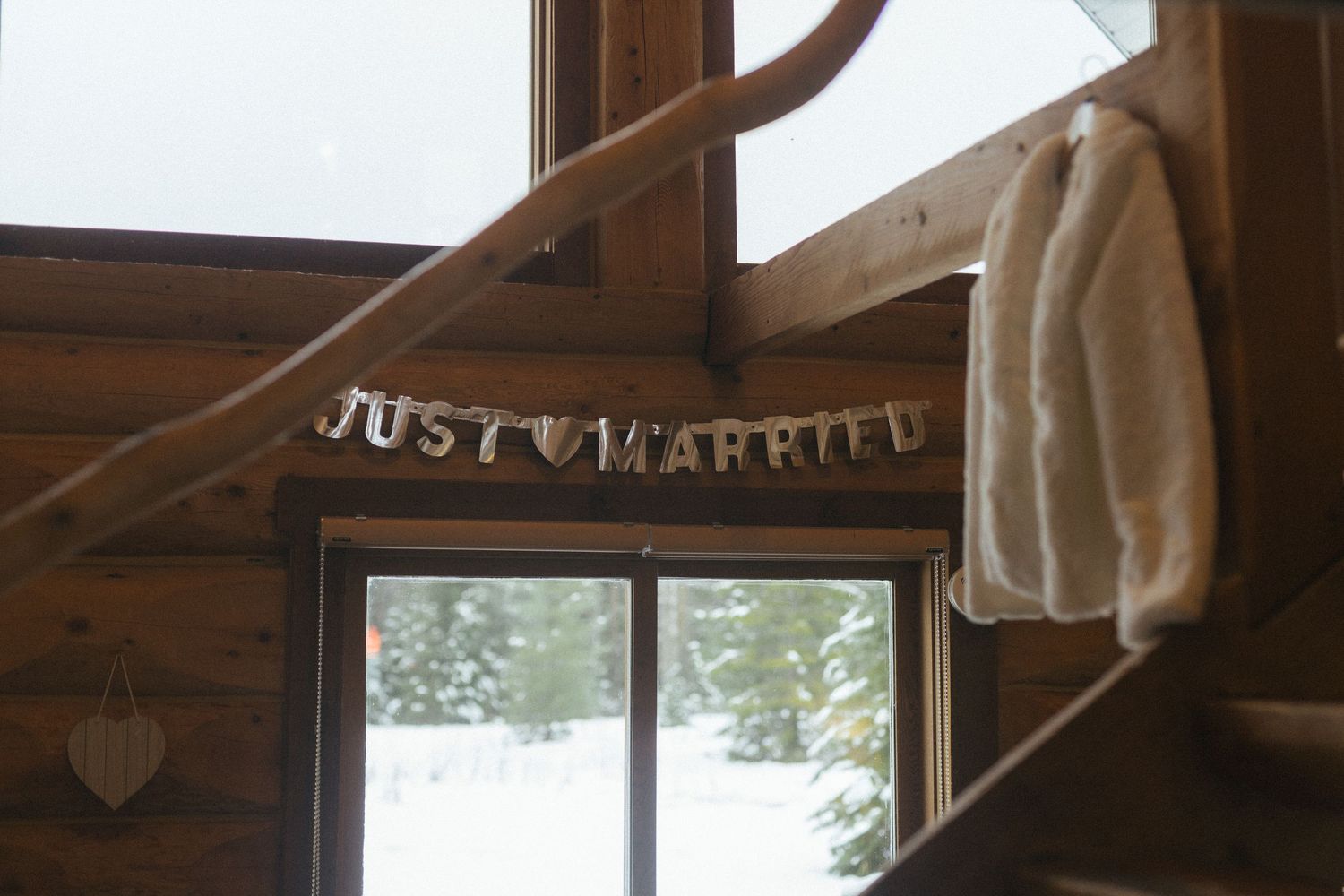 a fur jacket hangs from a hook in a cedar log cabin with a "just married" sign hung in the background