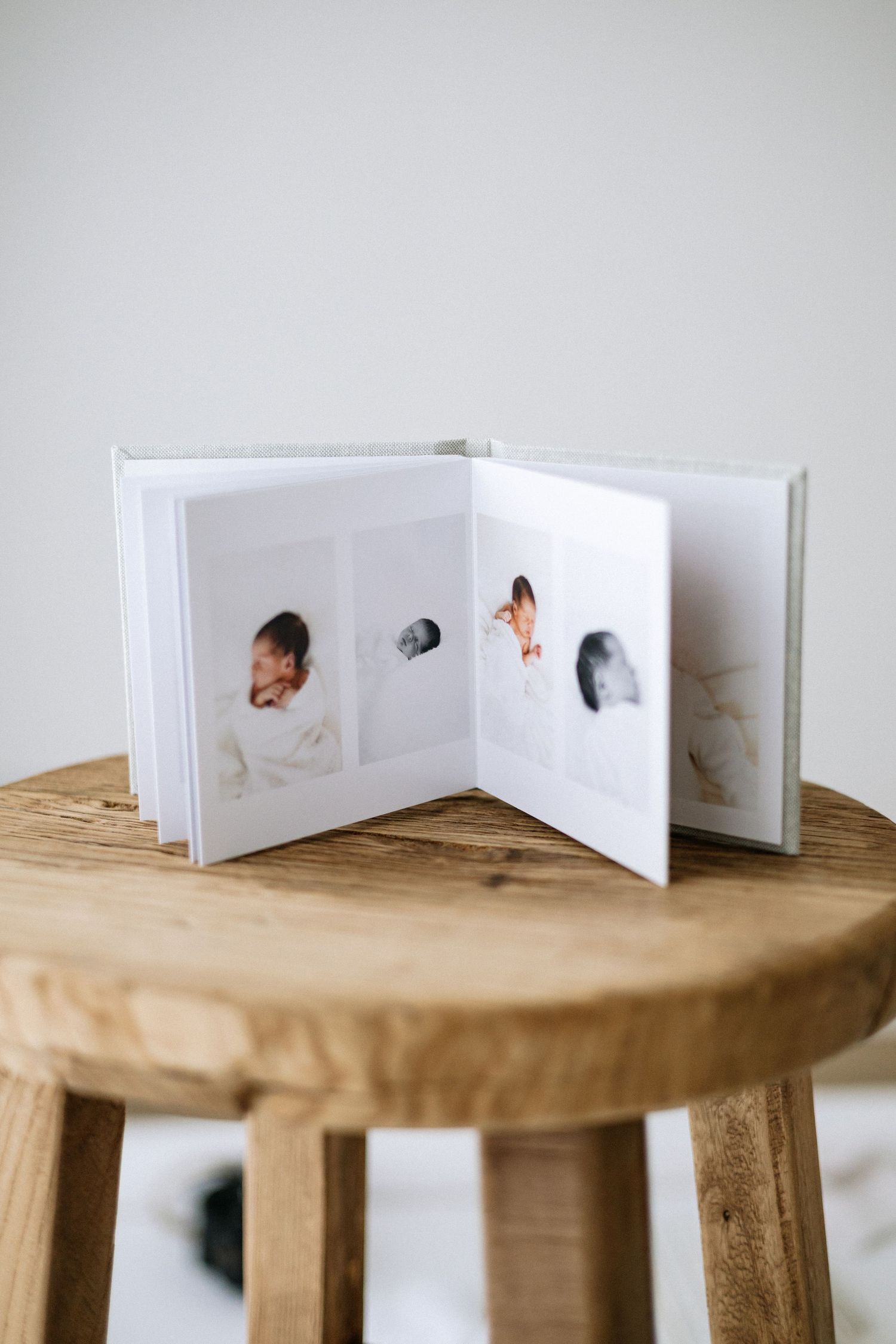 Open photo album with newborn baby portraits displayed on wooden stool against white wall Nottingham natural newborn and family photographer