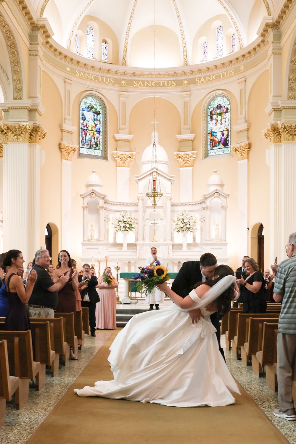 Bride and groom share a dip kiss in a stunning ornate church aisle after their wedding ceremony.