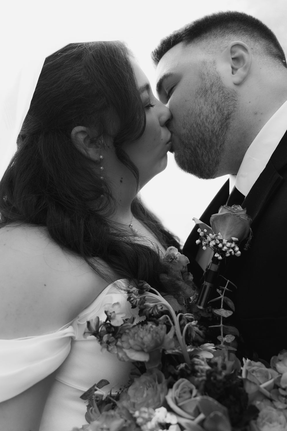 Black and white photo of bride and groom sharing a romantic kiss on their wedding day.