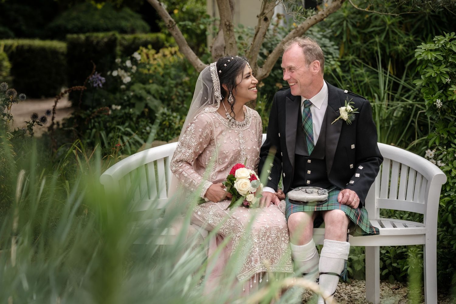 A couple in wedding attire walks together through a lush garden setting during their Islington ceremony.