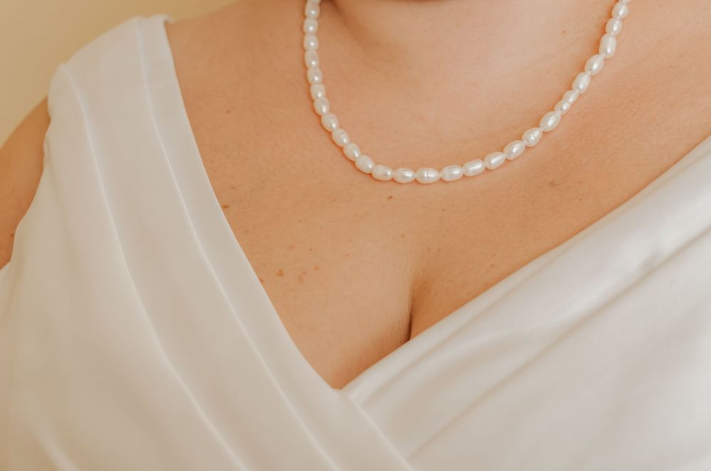 Close-up of a bride wearing a delicate freshwater pearl necklace with a white V-neck wedding dress.