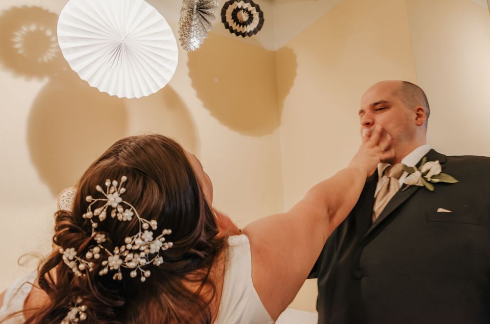 Bride feeding wedding cake to groom at reception, bride wearing elegant floral hair accessories.