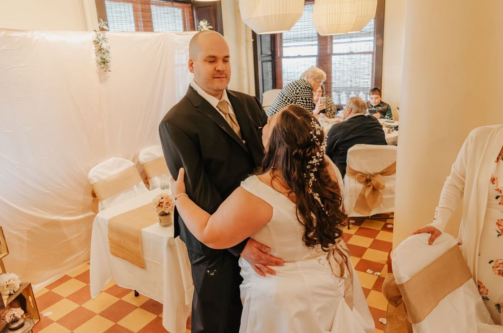 Bride and groom share first dance in elegant wedding venue with draped white fabric and decorated chairs.