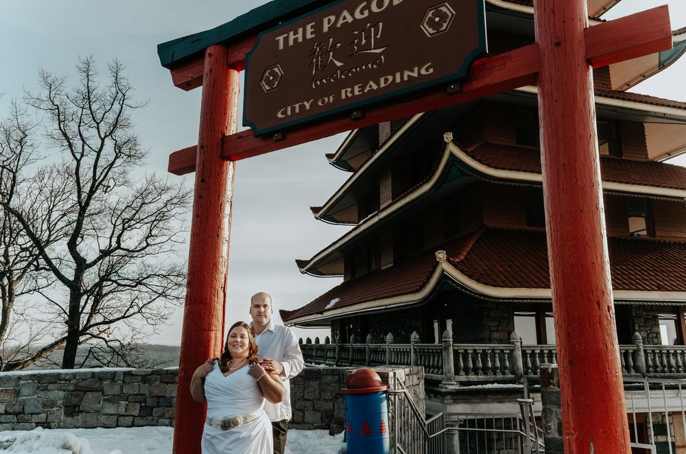Couple poses under red torii gate at The Pagoda, City of Reading, PA, in winter with snow-covered ground.