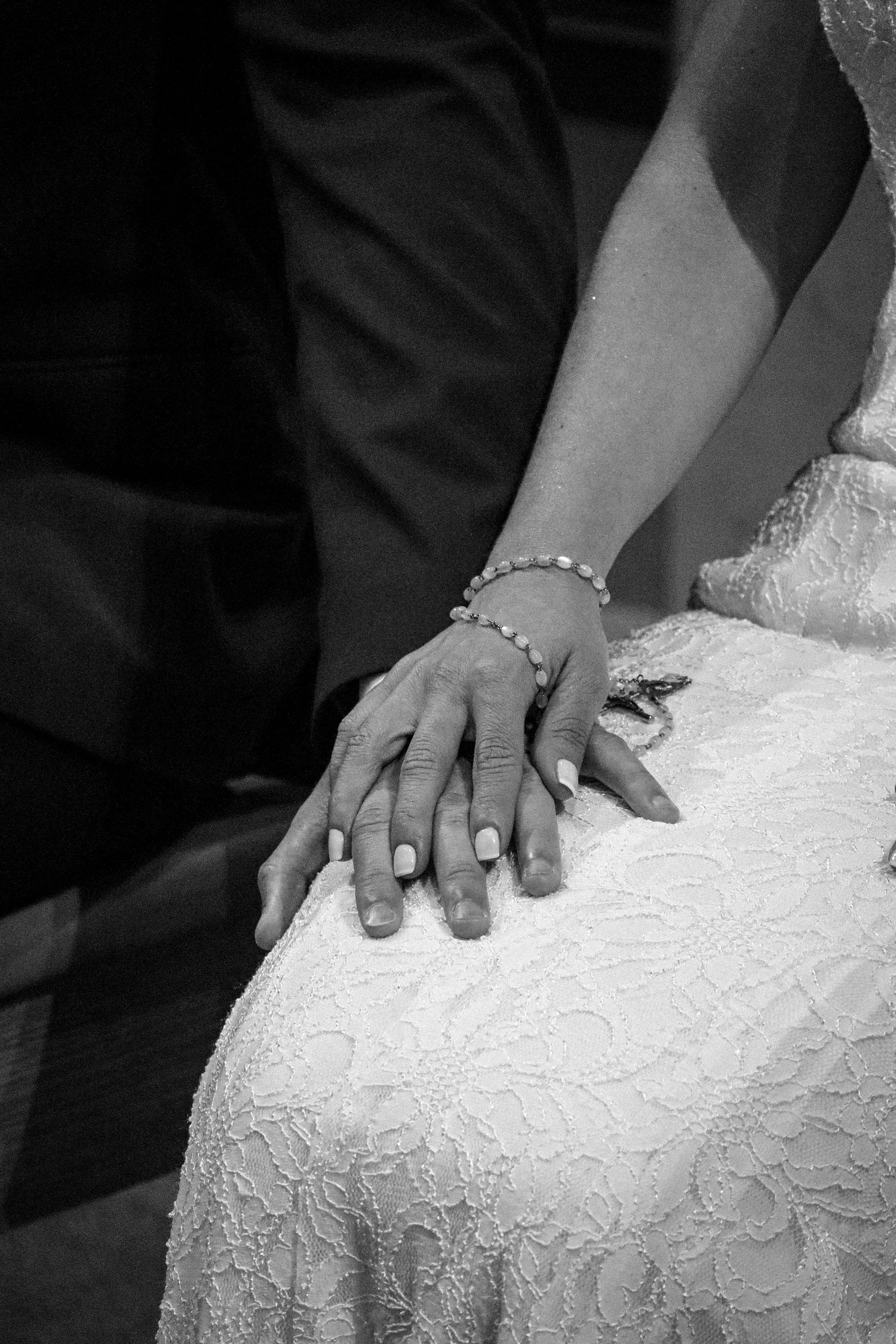 Close-up of hands resting on white lace wedding dress fabric.