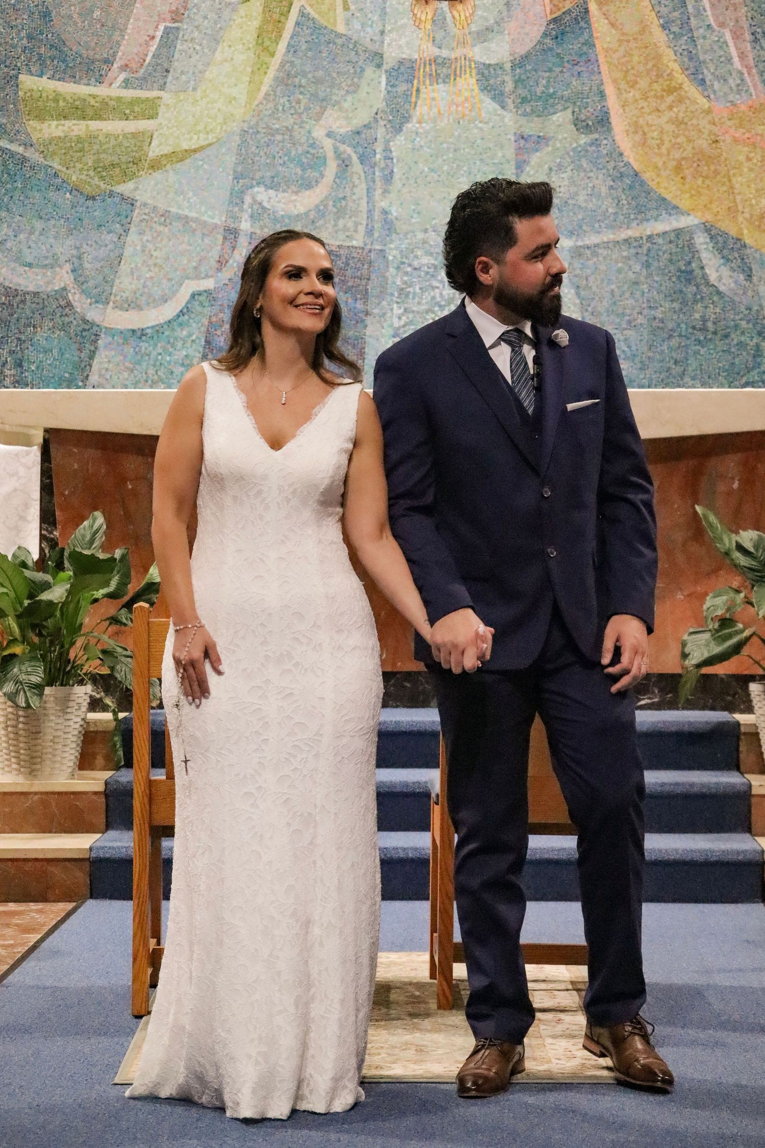 Couple in navy suit and white dress sitting together during wedding ceremony.