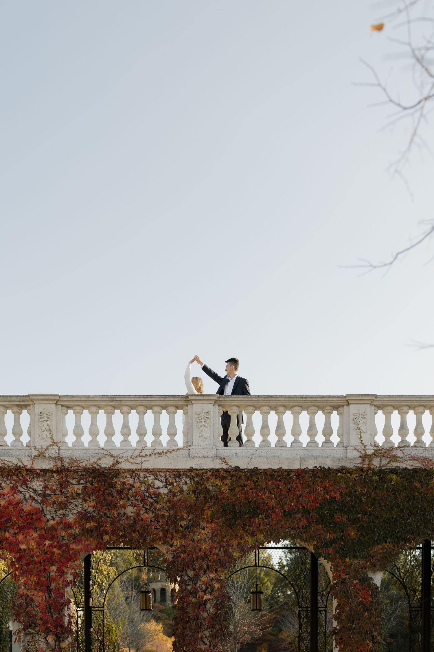 Bride and groom dancing on a white balustrade terrace surrounded by vibrant autumn foliage.
