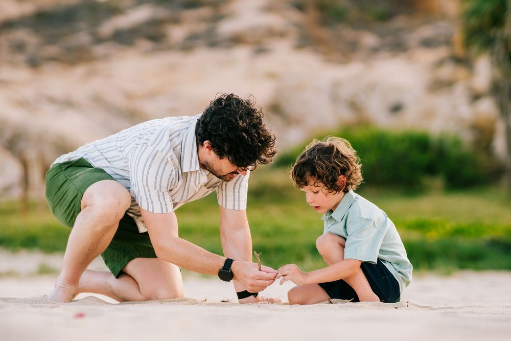 Father and young son playing together in the sand on a sunny beach day.