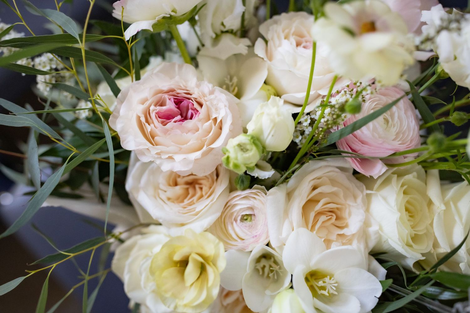 Lush bridal bouquet of blush and white roses, ranunculus, and greenery in soft natural light.