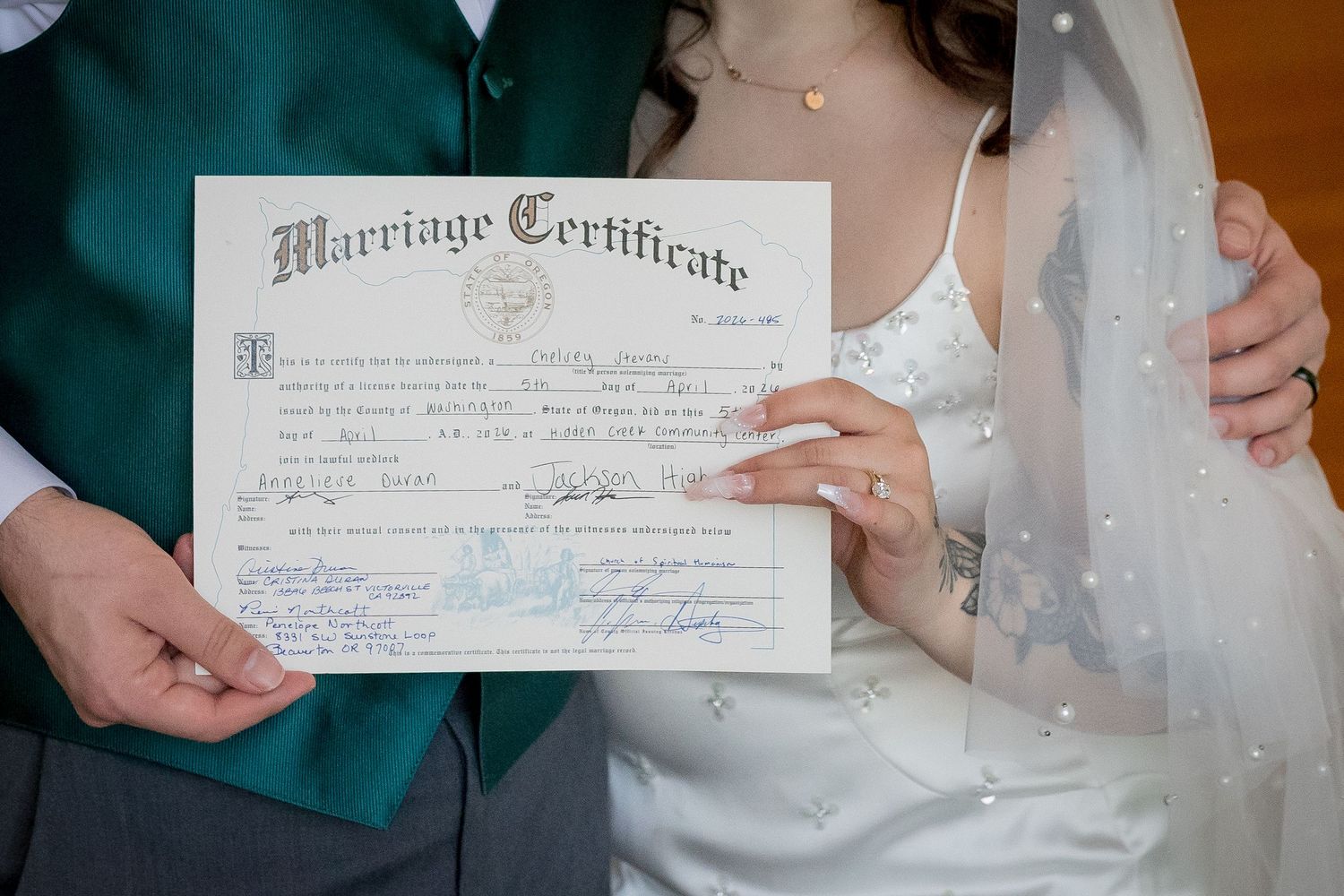 Bride and groom proudly displaying their signed marriage certificate, bride wearing a pearl veil.