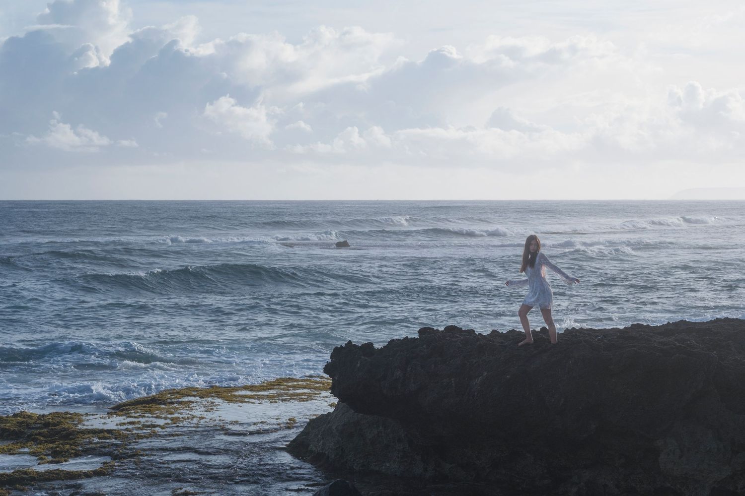 Woman standing on a rocky coastline overlooking the Pacific Ocean during a lifestyle portrait session on Oahu's North Shore.
