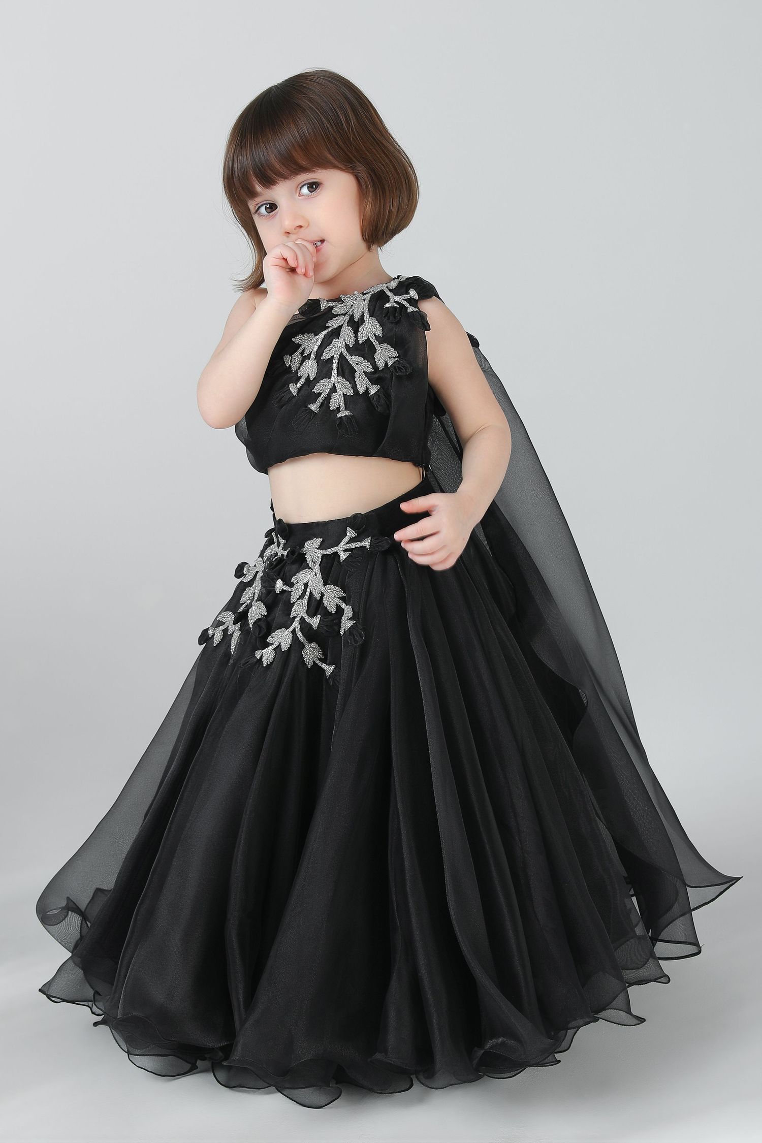 Young girl in plaid blazer and skirt with white tights and black bow headband, posing playfully.