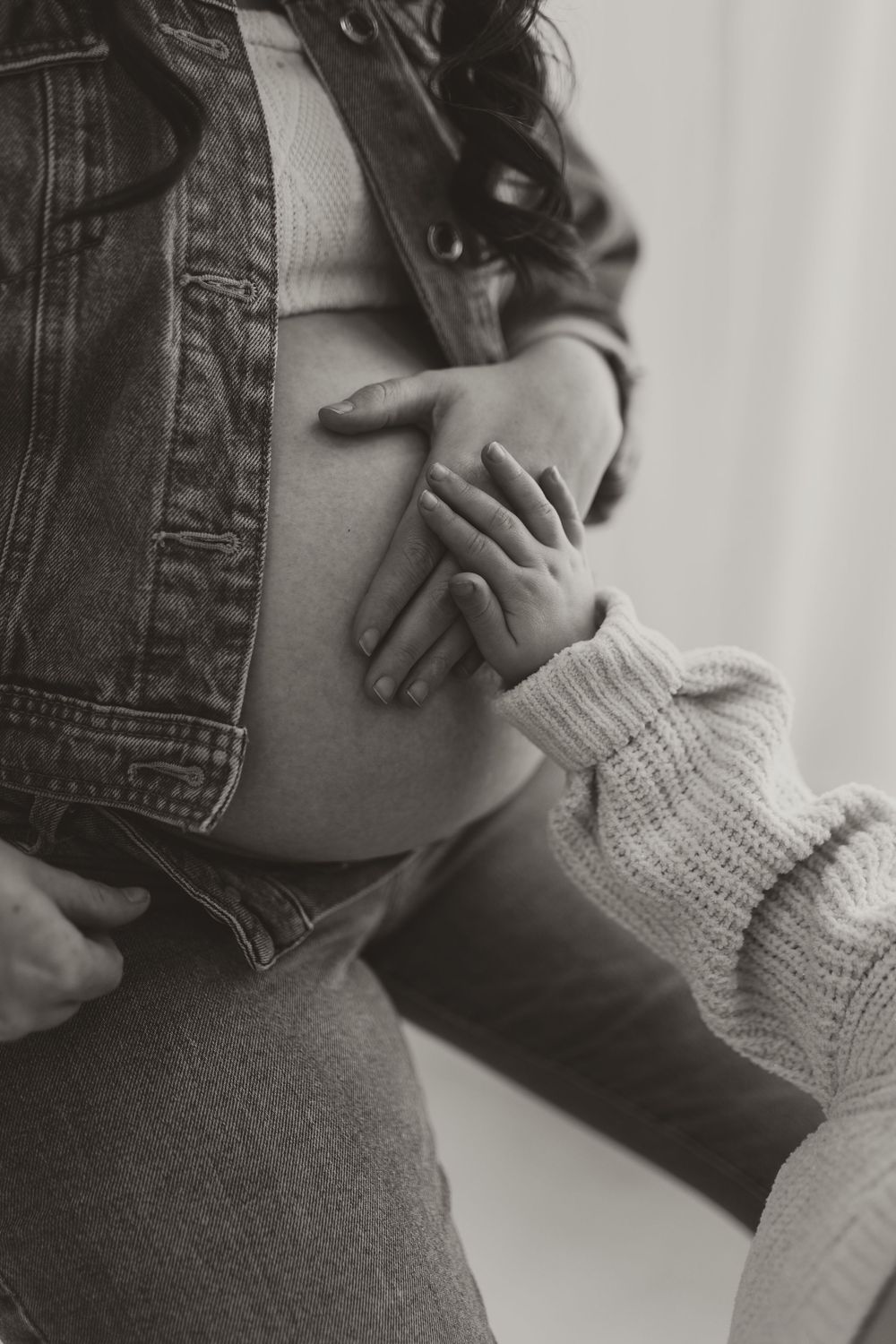 Black and white close-up of pregnant woman's belly with child's hand gently touching it.