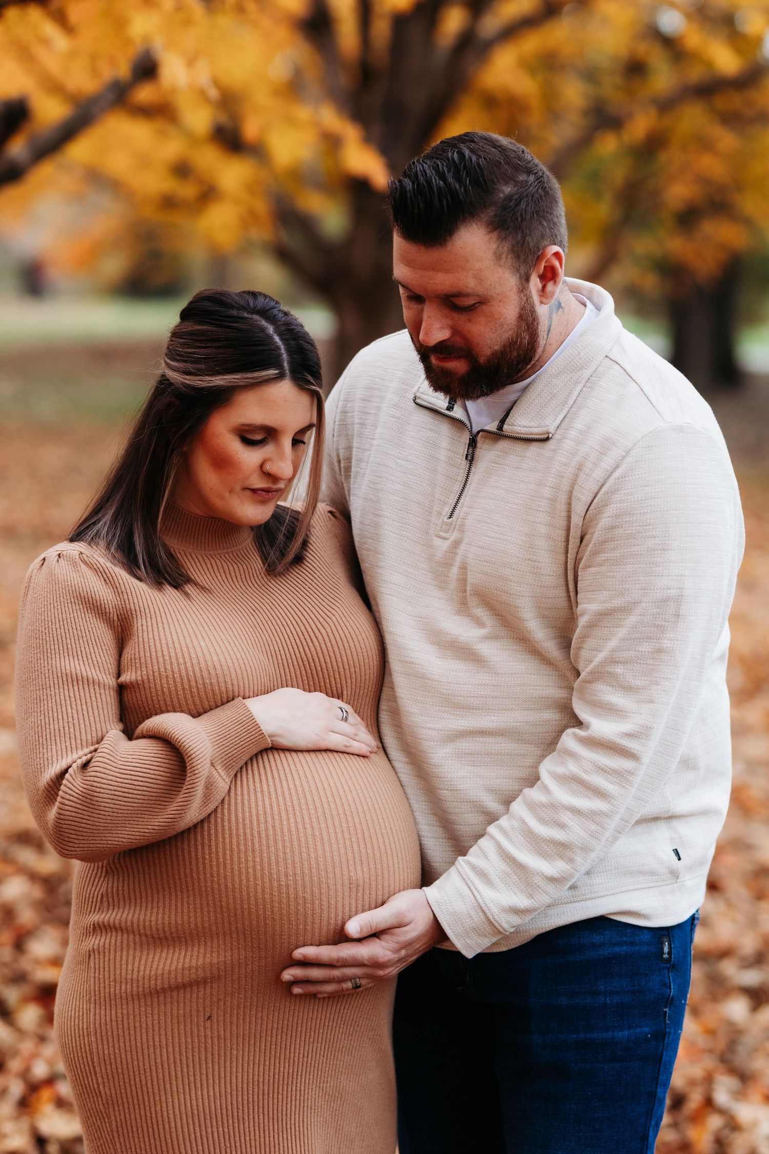 A couple tenderly cradles a pregnant belly together among colorful fall foliage in an outdoor maternity shoot.