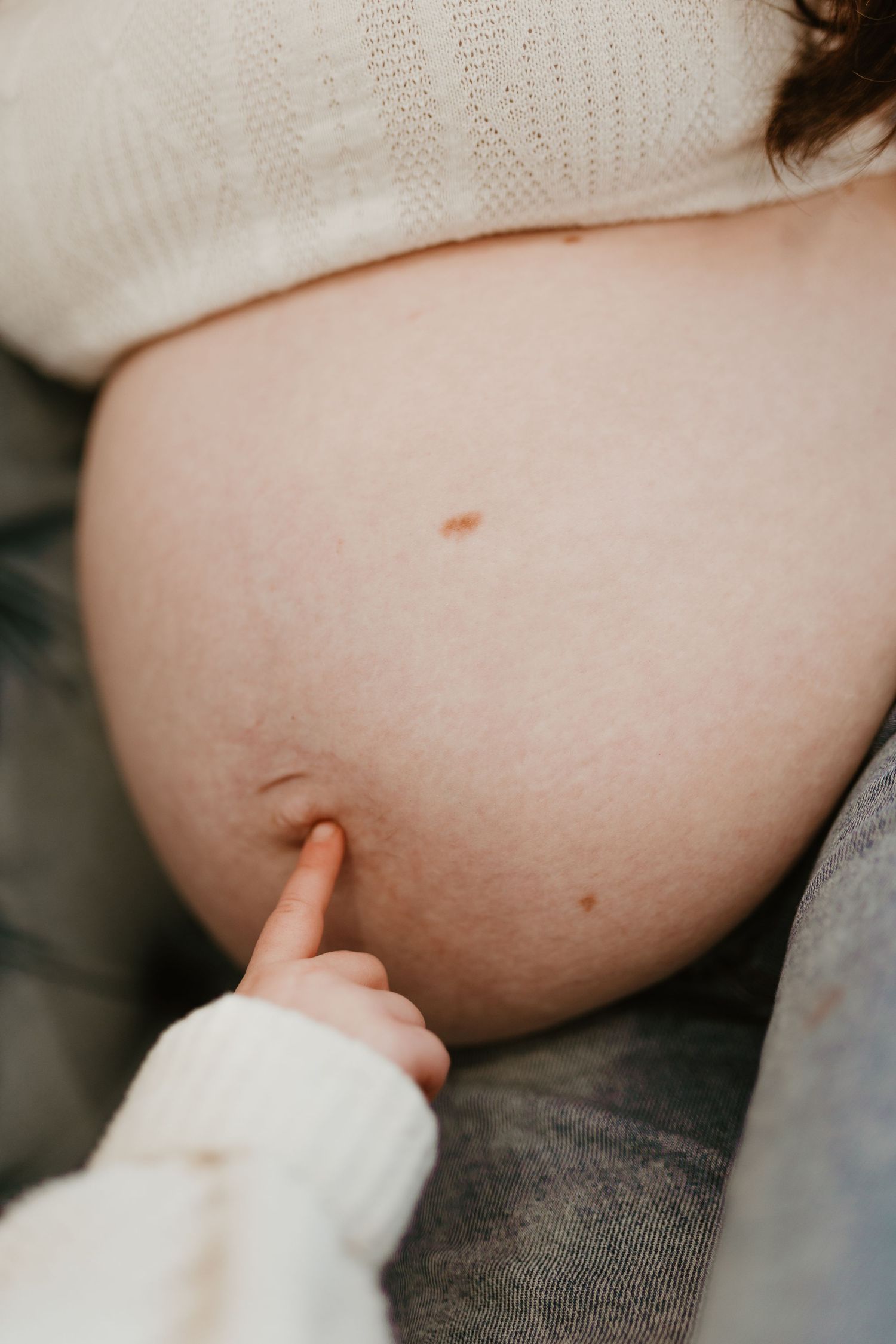 Close-up of a pregnant belly being gently touched by a small child's finger during a maternity photo session.