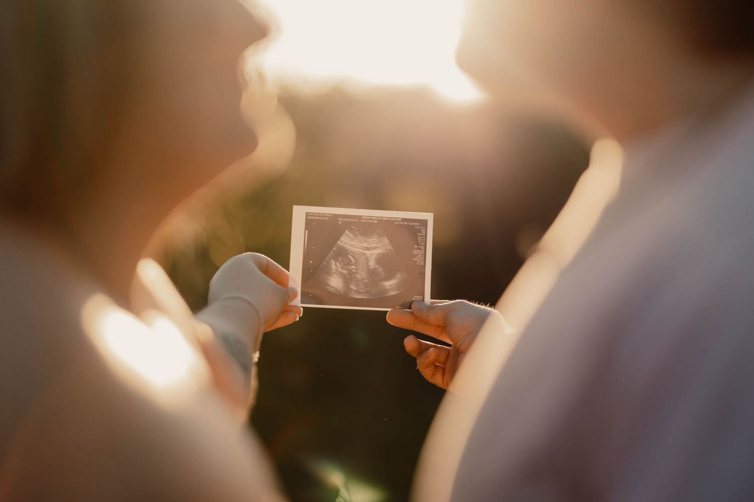 Couple looking at baby ultrasound photo together in warm golden sunlight during maternity photography session.
