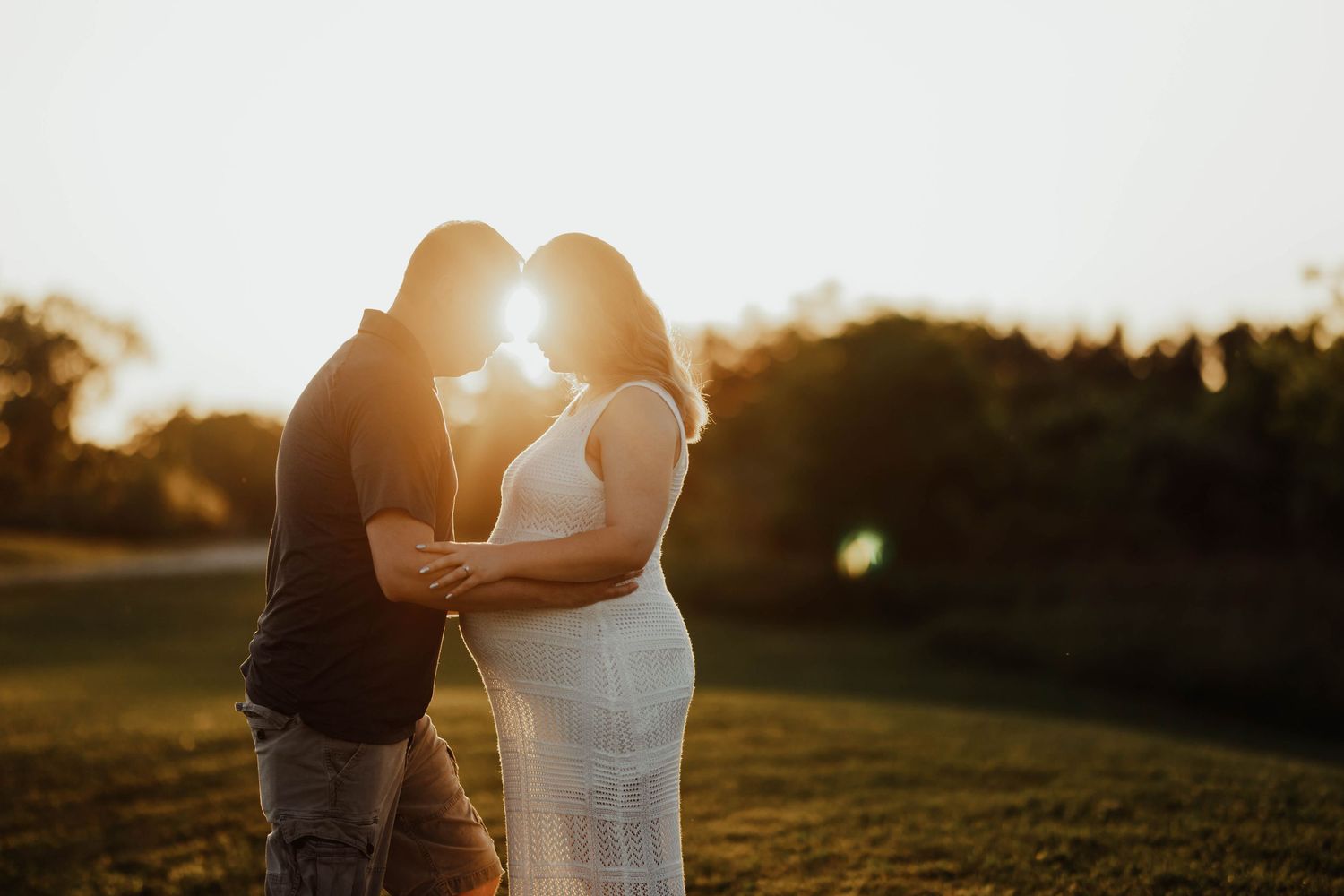Couple sharing a romantic moment at golden hour sunset in an outdoor maternity photo session.