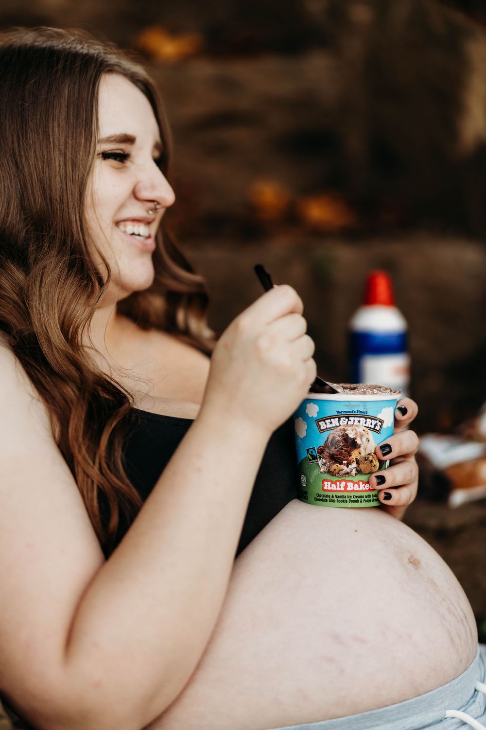 Smiling pregnant woman eating Ben & Jerry's Half Baked ice cream outdoors during a maternity photo shoot.