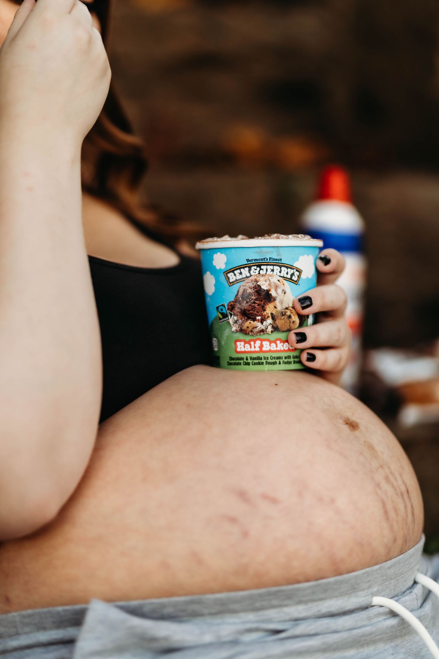 Close-up of pregnant belly with woman holding Ben & Jerry's Half Baked ice cream pint with dark painted nails.