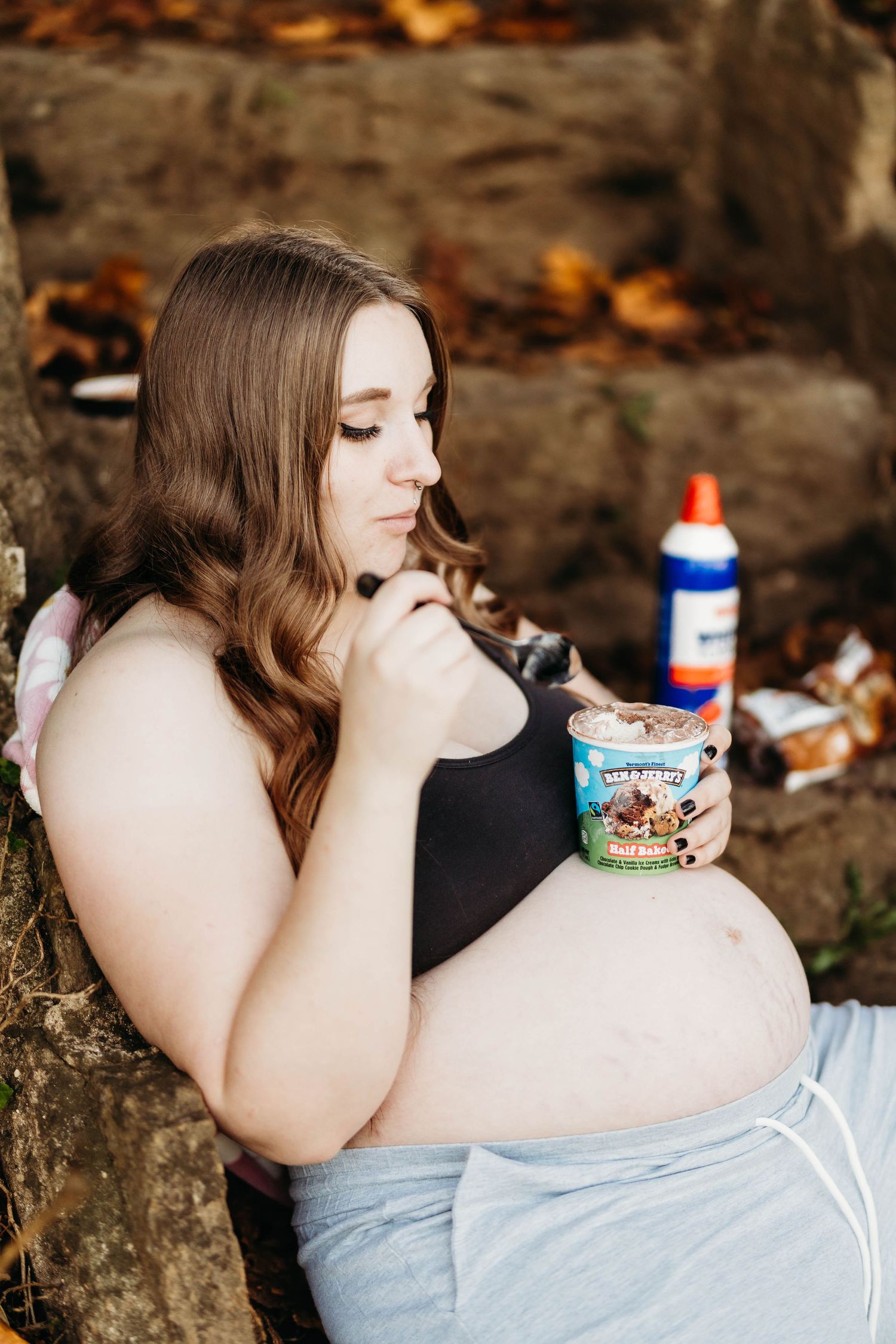 Pregnant woman sitting against a rock eating Ben & Jerry's ice cream during an outdoor maternity session.