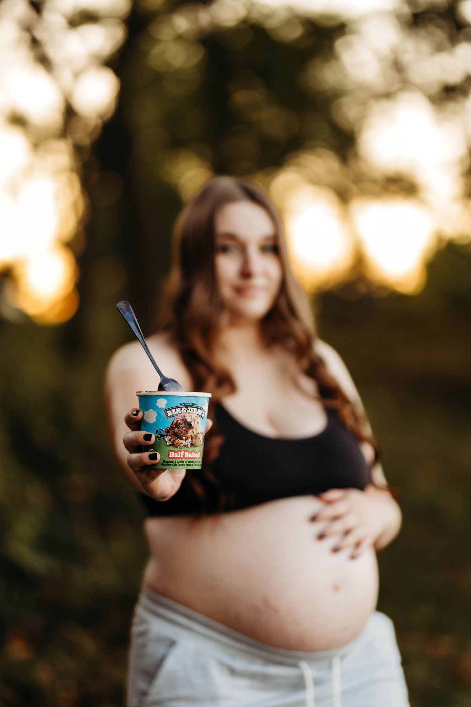 Pregnant woman offering Ben & Jerry's Half Baked ice cream to camera during golden hour maternity shoot.